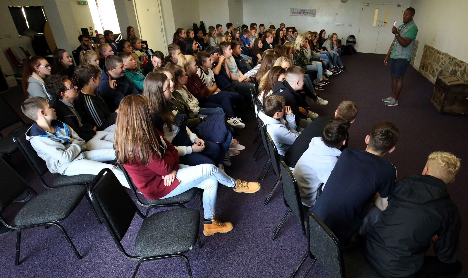 A man stands talking to a group of seated school pupils during an assembly