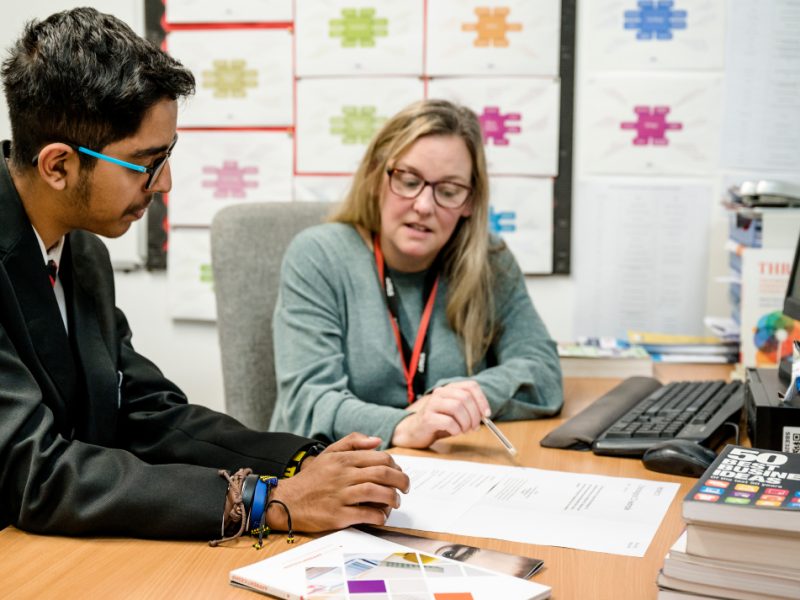 A careers adviser sat at a desk with a school pupil going through a written document