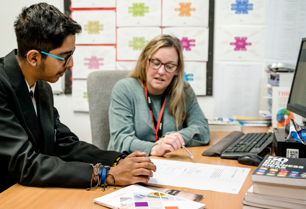 A careers adviser sat at a desk with a school pupil going through a written document