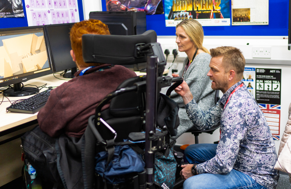 A student sat at a computer in conversation with an employee as part of their work experience placement