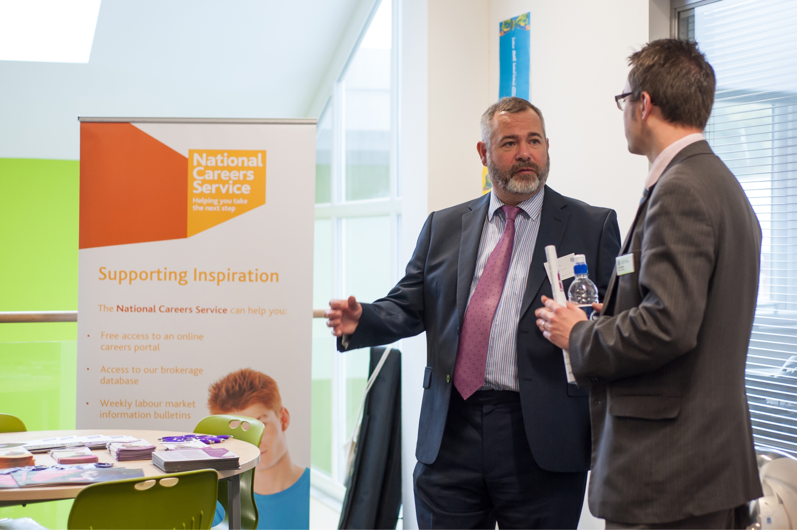 Two employees speaking in front of a National Careers Service banner at an employment fair