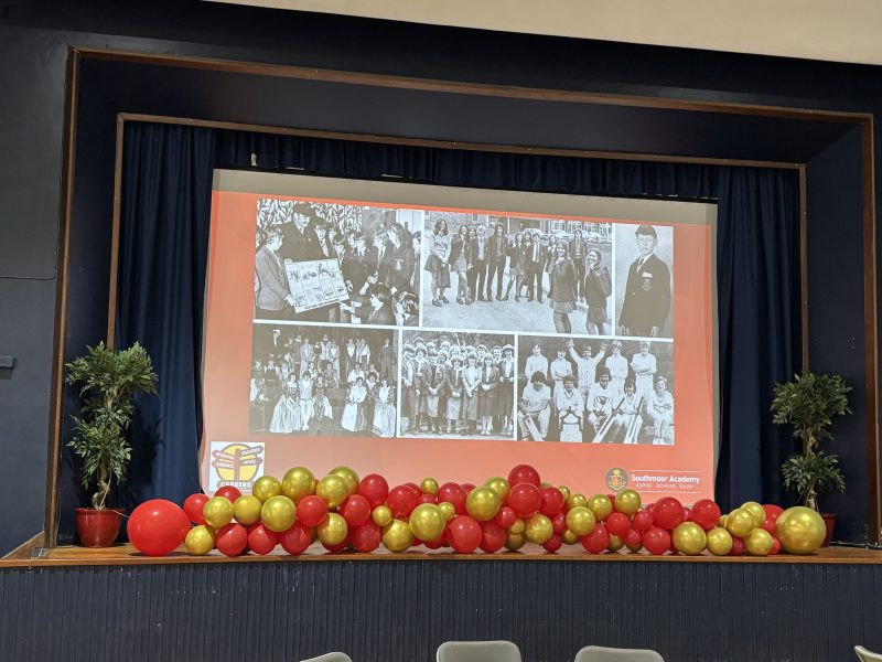 A projected screen in a school hall showing a collage of photos of former students from Southmoor Academy