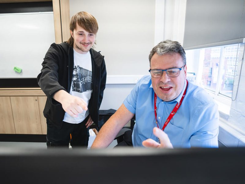 A young man and his teacher smiling together and looking at a screen