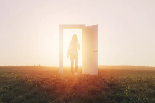 A young woman walking through a doorway into the sunshine